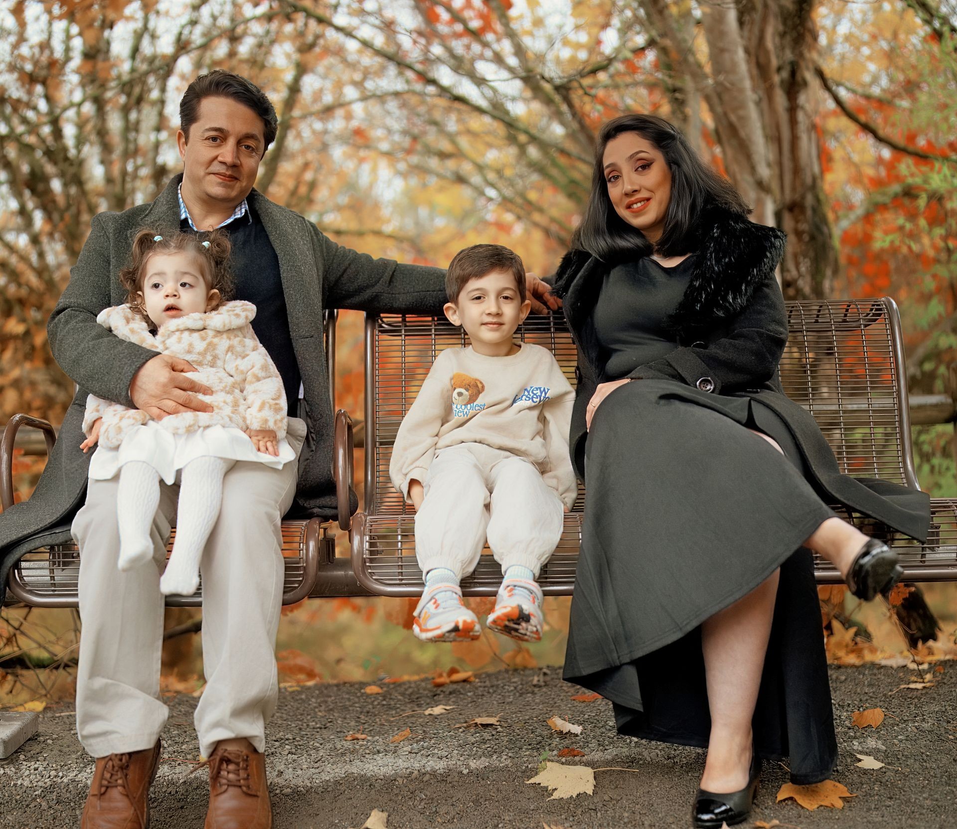 Family sitting on a park bench with autumn trees in the background.