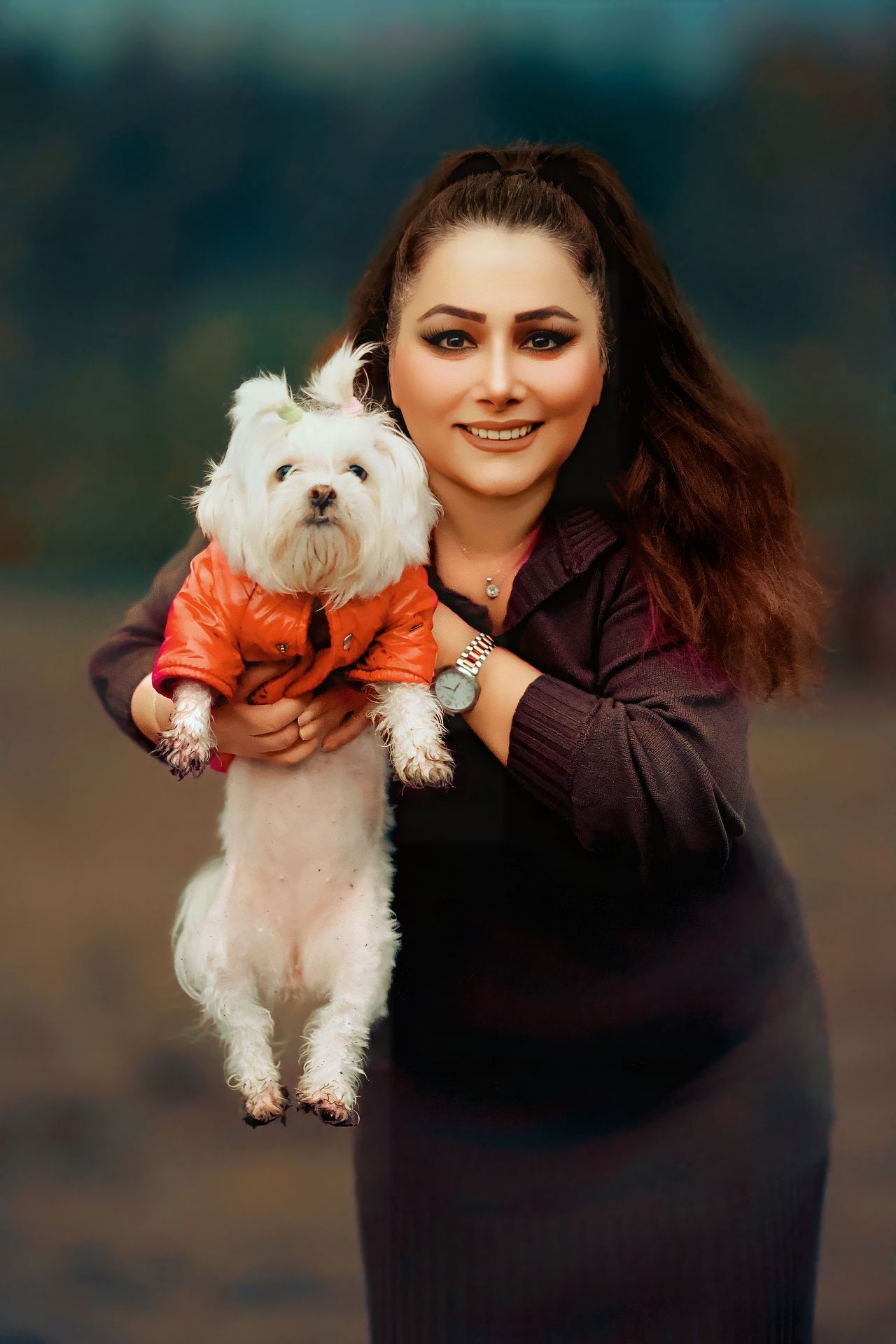 Smiling person holding a small dog in an orange jacket.